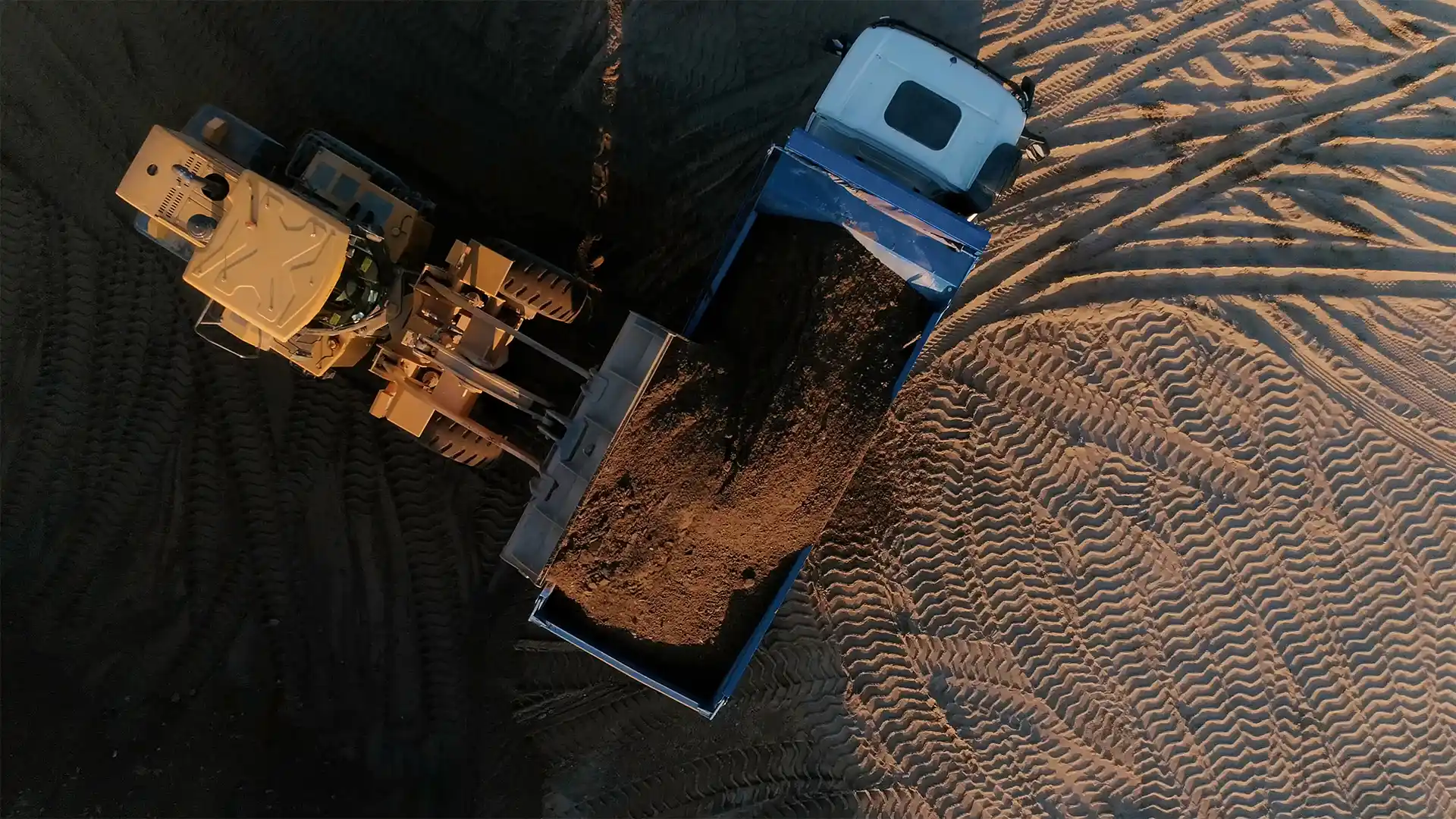 Aerial view of a front-end loader dumping soil into a mining truck at an open-pit mining site.