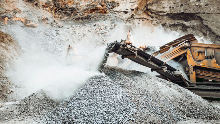 Industrial stone breaker rock crusher processing granite rocks at a quarry.